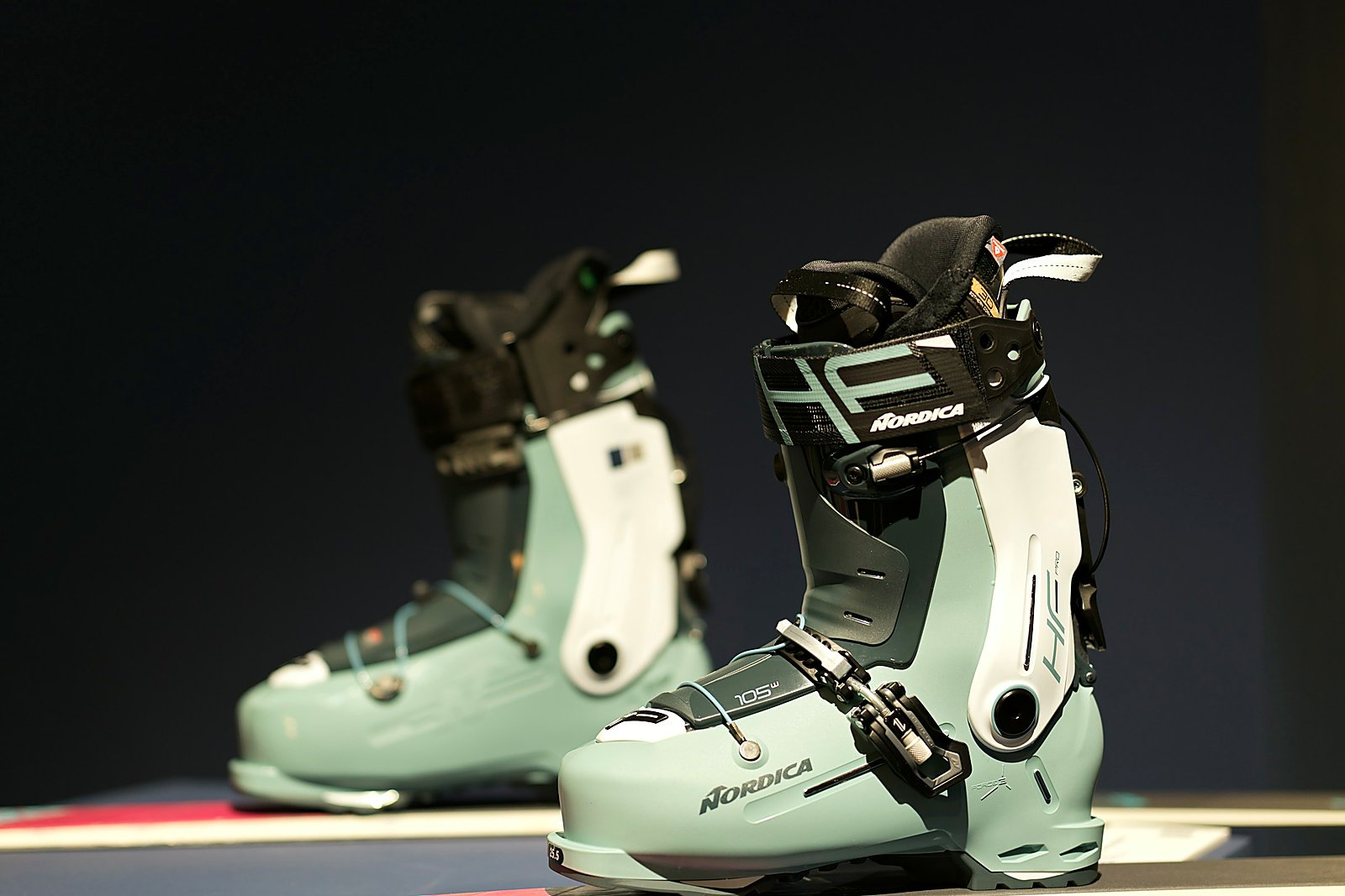 Pair of sage ski boots staged on a dark retail fitting display.